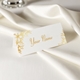 Personalised wedding place card with your name in elegant design on folded white cardstock. Set on a softly draped ivory tablecloth, creating a sophisticated and timeless look.