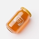 Clear glass jar filled with golden liquid, lying on its side with a gold screw lid and a round transparent label featuring white print and laurel wreath design. Ideal for customised or personalised branding on honey, preserves or condiments.