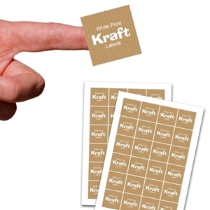 A square kraft label with white print reading White Print Kraft Labels is held on a fingertip above two full sheets of matching customised stickers. Each sheet contains multiple brown labels with subtle vertical stripes and white text, ideal for packaging or branding.