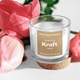 Glass candle jar with a personalised kraft label reading 30mm Square Stickers, White Print, Kraft Labels, 48 Stickers Per Sheet. The jar sits on a cork base, surrounded by pink peony flowers on a white background. Ideal for custom sticker or label product photography.