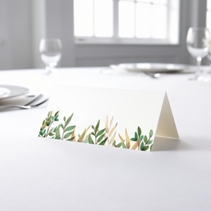 blank wedding place card with an elegant design printed on folded white cardstock, ready to write your names. Placed on a table set for a formal event, with plates, cutlery, and wine glasses in the softly blurred background.