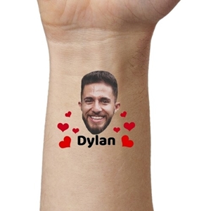 Close-up of an arm featuring a temporary tattoo of a smiling man's face surrounded by red hearts and the name 