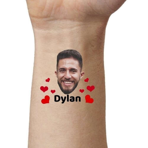 Close-up of an arm featuring a temporary tattoo of a smiling man's face surrounded by red hearts and the name 