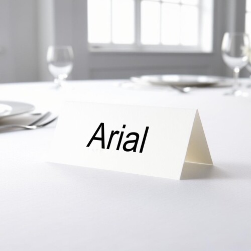 Personalised wedding place card with your name in elegant black script on folded white cardstock. Placed on a table set for a formal event, with plates, cutlery, and wine glasses in the softly blurred background.