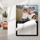 An A4 wall calendar for May 2025 with a sleek black design. The page features a family photo of a man with three children in a park, with a monthly grid below. The calendar is spiral-bound with a hanging hook and is displayed on a white wall in a modern room.