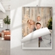Wall planner calendar hanging on a white wall in a bright living room. The page features a festive family photo with a woman, man, and young boy smiling in front of a rustic wooden backdrop with fairy lights and a Christmas tree. The calendar page is partially turned, revealing lined date entries below the photo.