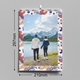 Wall calendar featuring a scenic photo of a couple holding hands by a mountain lake, framed with a colourful leaf pattern. Dimensions are clearly shown as 297mm in height and 210mm in width (A4 size). A metal wire binding and hanging hook are visible at the top, highlighting the calendar's practical design for easy wall display.