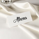 Personalised wedding place card with your name in elegant black script on folded white cardstock. Set on a softly draped ivory tablecloth, creating a sophisticated and timeless look.