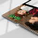 Close-up of a personalised wall calendar featuring a festive photo of a baby wearing glittery green reindeer antlers and lying next to an adult in a red flannel shirt, with a decorated Christmas tree blurred in the background. The calendar is wire-bound with a metal hanging loop, resting on a white surface in natural daylight.