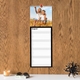 A customisable black kitchen calendar displayed on a wooden wall. The August page is shown with space for notes and a photo of your choice, a white shelf holds a candle, sunglasses, and decor