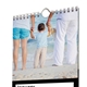 Close-up of a customisable kitchen calendar showing part of the January page. The featured photo depicts a child holding hands with two adults while standing on a beach, facing the sea. The child is holding a soft toy in one hand.