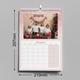 An A4 pink glitter-themed photo calendar displaying the July 2025 page. The picture shows a young child kissing a baby on a white bench. The calendar is wire-bound, measuring 420mm by 297mm, with a month grid layout.