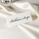 Personalised wedding place card with your name in elegant black script on folded white cardstock. Set on a softly draped ivory tablecloth, creating a sophisticated and timeless look.