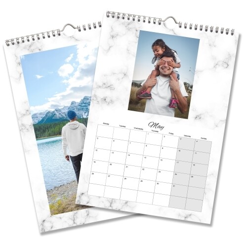 Two A4 wall calendars with marble-patterned borders. One features a landscape image of a person by a lake and mountains, while the other shows May 2025 with a photo of a man carrying a child on his shoulders. Both calendars have spiral bindings and hanging hooks.