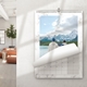 An A4 wall calendar with a marble design, displaying a photo of two people standing by a lake with snowy mountains in the background. A page is being turned, revealing part of a monthly grid. The calendar is mounted on a white wall in a bright room with modern decor.