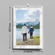 A 2026 wall calendar with a white marble border is displayed hanging on a grey wall. The cover features a couple holding hands by a lake, facing snowy mountain peaks under a bright sky. The calendar measures 210mm wide by 297mm tall (A4 portrait) and includes a spiral binding with a central hanging hook for easy wall display.