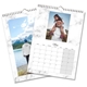 Two A4 wall calendars with marble-patterned borders. One features a landscape image of a person by a lake and mountains, while the other shows May 2025 with a photo of a man carrying a child on his shoulders. Both calendars have spiral bindings and hanging hooks.