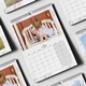 An A3 wall calendar for July 2025 with a marble design, featuring a photo of a young child gently kissing a baby on a rustic bench. The calendar has a monthly grid, spiral binding, and a hanging hook. Multiple calendar designs are displayed underneath.