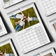 A 2026 wall calendar with a white marble border is open to September, featuring a photo of a family lying on green grass, smiling and dressed in white tops and jeans. The calendar grid shows clearly marked dates, and the spiral binding with a central hanging hook allows for easy wall display. Several other calendar pages are arranged around it, showcasing similar layouts and designs.