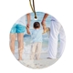 Round ceramic bauble with an image of a child standing between two adults at the beach, holding hands. The child wears beige trousers and a striped shirt, facing the sea. One adult is holding a teddy bear.