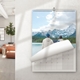 A 2025 A3 photo calendar hanging on a wall, showing a scenic image of two people standing by a lake with snow-capped mountains in the background. The current month page is partially turned over. A modern living room is visible to the left.