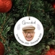 Round ceramic bauble hanging on a Christmas tree, featuring a photo of an elderly man with glasses and a beige cap. The word 