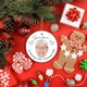 Round ceramic bauble featuring a photo of an elderly woman with glasses and white hair, surrounded by holiday decorations like a gingerbread figure, ornaments, and pinecones. The word 