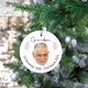 Round ceramic bauble hanging on a Christmas tree, featuring a photo of an elderly man with short grey hair and a beard. The word 