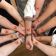 A group of people standing in a circle, each extending their forearm inward to form a star shape with hands linked. Each forearm displays a red star-shaped temporary tattoo with a face and the words Happy Birthday!