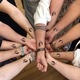 A group of people join their forearms together in a circle, each wearing temporary tattoos featuring a face with a party hat. The image showcases unity and celebration, with each tattoo adding a playful, personalised touch.