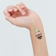 Close-up of a person's wrist with a temporary tattoo featuring a man's face wearing a green party hat that reads 