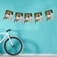 Personalised photo bunting with a couple dressed in wedding attire, displayed against a vibrant blue wall with a bicycle resting nearby.