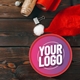 Red chocolate tub with a customisable circular sticker featuring the text Your Logo in bold white font on a purple gradient background, placed on a wooden table with Christmas wrapping supplies and a Santa hat.