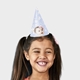 Smiling girl wearing a light blue personalised party hat featuring a baby girl's face with a pink floral headband, decorated with white daisies and the number 1, designed for a first birthday celebration.