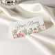 Personalised wedding place card with your name in elegant design on folded white cardstock. Set on a softly draped ivory tablecloth, creating a sophisticated and timeless look.