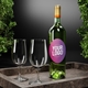 Green wine bottle with a personalised oval label featuring a pink-to-purple gradient and placeholder text Your Logo. The bottle is placed on a stylish tray alongside two empty wine glasses. The background includes green foliage, creating an elegant and sophisticated setting. Ideal for customised branding or personalised gifts.