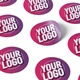 Custom circular and irregular-shaped stickers featuring Your Logo text in bold white font on pink and purple backgrounds, displayed on a white surface with a shadow effect.