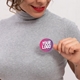 A woman wearing a grey turtleneck holds a round, personalised sticker with a pink gradient background and the words 