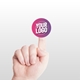 Close-up of a hand holding a small, personalised circular label with a custom logo on the fingertip, set against a light background. The label is pink and purple with the text Your Logo in white.