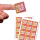 Close-up of a hand holding a small square custom sticker with bold text in pink, white, and yellow on a kraft background. Two sheets of identical stickers are displayed below. Perfect for personalised labelling and branding