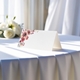 blank wedding place card printed with an elegant design on folded white cardstock ready to write your names on. Displayed on a table with a flowing white tablecloth, with soft natural light and white roses in the background.