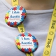 Close-up of two round badges pinned to a yellow lanyard with a white tshirt behind. The badges display a colourful jigsaw puzzle pattern with text reading 