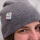 A close-up of a round badge pinned to a grey knit hat worn by a person. The badge displays a colourful jigsaw puzzle pattern with text reading 