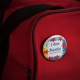 A round badge pinned to a red backpack. The badge features a colourful jigsaw puzzle pattern with text reading 