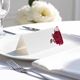 blank wedding place card with elegant design on folded white cardstock. Placed on a white plate with silver cutlery and a neatly folded napkin, with soft-focus white flowers in the background.