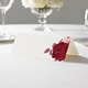 wedding place card with an elegant design on folded white cardstock ready to write your name on. Displayed on a white tablecloth with wine glasses, plates, and a floral centrepiece in the softly blurred background.