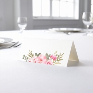 blank wedding place card with an elegant design printed on folded white cardstock, ready to write your names. Placed on a table set for a formal event, with plates, cutlery, and wine glasses in the softly blurred background.