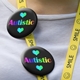 Close-up of two round badges pinned to a yellow lanyard with a white tshirt behind. The badges display a a black background featuring the word 