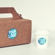 Kraft takeaway box and white coffee cup, each featuring a transparent circle label with a custom blue and white logo. The eco-friendly packaging highlights personalised branding for food or beverage businesses