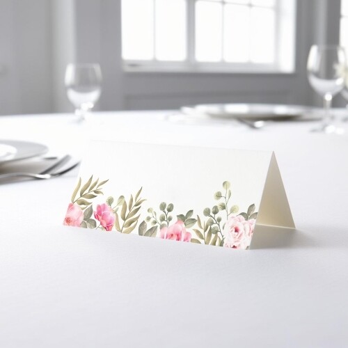 blank wedding place card with an elegant design printed on folded white cardstock, ready to write your names. Placed on a table set for a formal event, with plates, cutlery, and wine glasses in the softly blurred background.